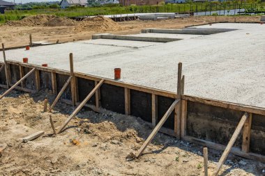 İşçiler, açık havada doğal manzarayla çevrili bir inşaat alanında beton bir temel oluşturuyorlar..