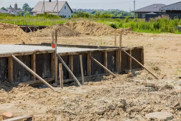 İşçiler, yeşillik ve evlerle çevrili bir inşaat alanında ahşap destekli bir vakıf kuruyorlar..