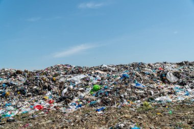 Açık mavi gökyüzü altında çeşitli atık türleriyle dolu büyük bir atık alanı etkili atık yönetimi uygulamalarına duyulan acil ihtiyacı gösteriyor.