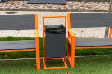 Parlak turuncu aksanlı yeni dizayn edilmiş banklar kamu alanındaki siyah bir çöp kutusunu kuşatarak temizliği ve rahatlığı teşvik ediyor..