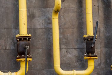 Kapakçıklı iki sarı sanayi borusu gri bir duvara monte edilir ve şehir ortamında işlevsel bir tasarım sergiler..