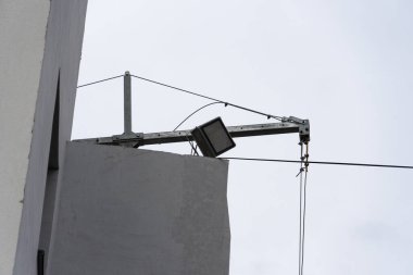 Gündüz koşulları altında gri yüzeye ışık saçan, binadan yayılan metal bir desteğe spot ışığı konur..