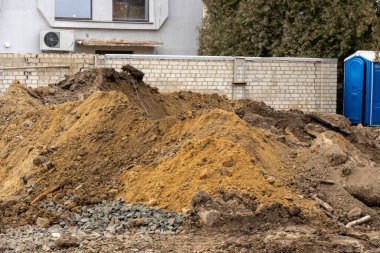 İnşaat işçileri mahallede yeni konut projeleri başlatmak için büyük toprak ve çakıl yığınları olan bir site hazırlıyorlar..