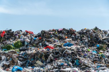 Naylon torbalar ve temiz bir gökyüzünün altında atılan malzemeler de dahil olmak üzere çeşitli atıklarla dolu geniş bir arazi alanı..