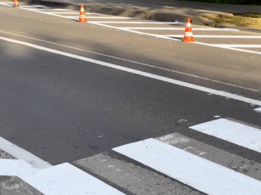 Trafik konileri, temiz gökyüzünün altındaki bir şehir caddesinde yeni boyanmış yaya geçidine yerleştiriliyor..