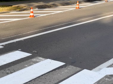 Trafik konileri, parlak güneş ışığı altında kentsel çevrede güvenliği artıran yaya geçidinde devam eden yol çalışmalarını gösteriyor..
