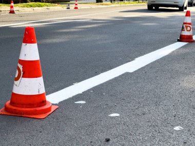 Trafik konileri ve yoğun bir caddede gündüz saatlerinde yeni boyanmış beyaz çizgilerle yol çalışması yapılıyor..