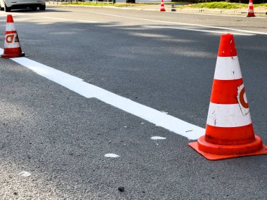 Trafik konileri, bir kamu parkının yakınındaki gündüz yol çalışması sırasında banliyö yolunda yeni boyanmış şeridi gösteriyor..