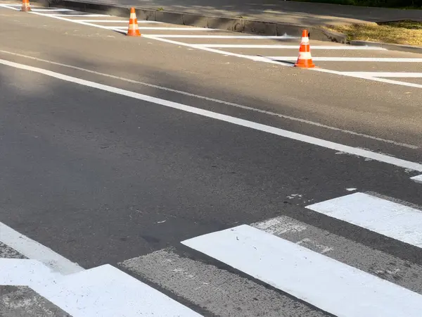 Trafik konileri, temiz gökyüzünün altındaki bir şehir caddesinde yeni boyanmış yaya geçidine yerleştiriliyor..