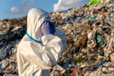 Koruyucu dişli işçiler, gün ışığında açık mavi gökyüzünün altındaki atık sahasında büyük miktarda plastik atık biriktiriyorlar..