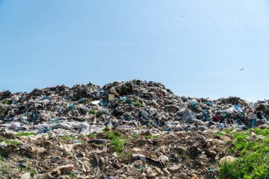 Büyük bir atık yığını mavi gökyüzünün altındaki bir atık sahasında, çevre ve atık yönetimi hakkında endişelere yol açıyor..
