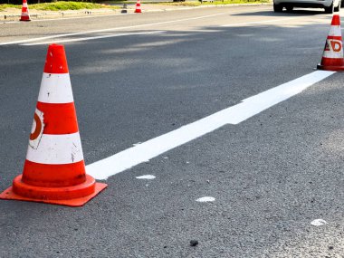 Trafik konileri hareketli bir şehir caddesinde taze boyanmış çizgiler boyunca gün içinde etraflarında arabalar dolaşır..