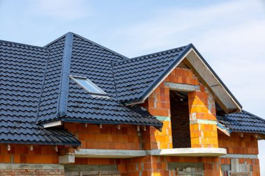 Gündüz vakti tamamlanmak üzere siyah kiremitli çatı ve tuğla duvarlı modern bir ev inşa ediliyor..