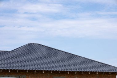 Açık mavi gökyüzünün altında, dağınık bulutlu, dokulu bir çatının detaylı bir görüntüsü, karoların karmaşık desenlerini ortaya çıkarır..