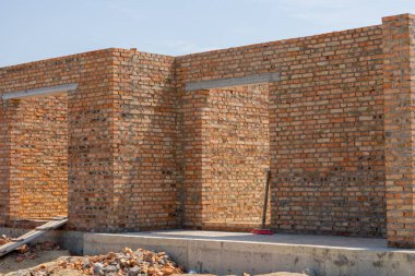 İşçiler, gün ışığında moloz ve aletlerle çevrili bir inşaat sahasına sağlam bir tuğla duvar inşa ediyorlar..