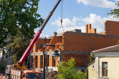 Turnalar tuğla bina yapımını desteklemek için malzeme taşırken, işçiler açık mavi gökyüzü ve parlak güneş ışığı altında bölgeyi yönetiyorlar..