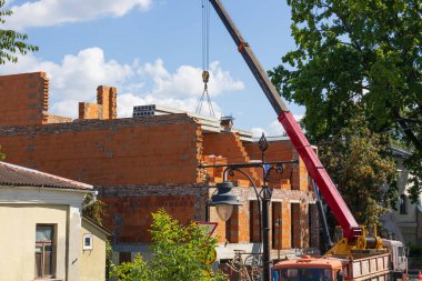 İşçiler, bir vincin temiz gökyüzünün altında yeni bir yapı inşa etmek için tuğla kaldırdığı bir inşaat sahasında meşguller..