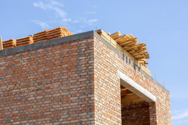 İşçiler, temiz bir gökyüzüne karşı tahta ve tuğla sergilenen tuğlaların dikildiği bir inşaat alanında meşguller..