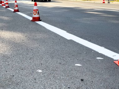Trafik konileri, geçen araçların güvenliğini sağlamak amacıyla bir inşaat projesi sırasında yolda yeni boyanmış beyaz bir çizgi çiziyor..