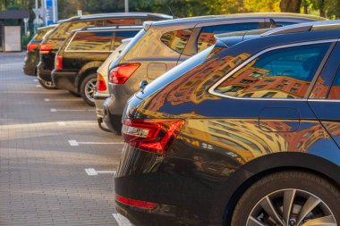 Şehir otoparkında park halindeki bir sıra araba öğleden sonra güneş ışığı altında yakındaki binaların yansımalarını sergiliyor..