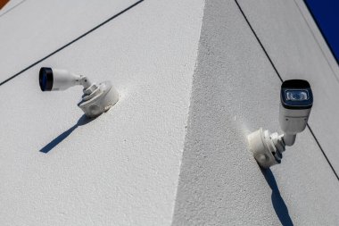 Beyaz bir binanın keskin bir köşesine yerleştirilmiş iki güvenlik kamerası gün boyunca çevredeki aktiviteleri kaydediyor..