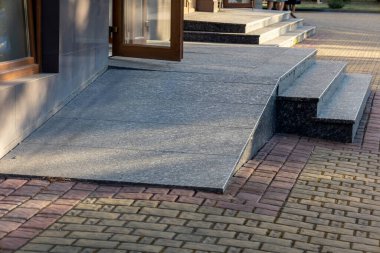 Parlak gün ışığı, ziyaretçiler için erişilebilirliği artıran çağdaş bir binanın girişine giden düz bir rampa ve adımları vurguluyor..