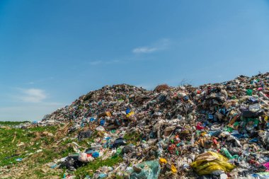Büyük bir çöp yığını açık gökyüzü ile kırsal bir alanda duruyor ve atık yönetimi ve kirlilik sorununu gözler önüne seriyor..