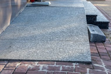 Gri taş kaldırım, güneşli bir günde binanın girişindeki bir dizi basamağa doğru yavaşça ilerliyor..