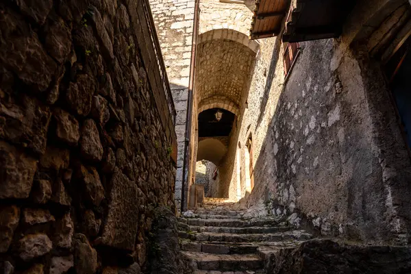 Zemin kattan yukarıya, kemer yolunun altından geçen taş bir merdivenin ve ışık ile gölge arasındaki güçlü zıtlıktan etkilenen taş duvarların arasına bakın.