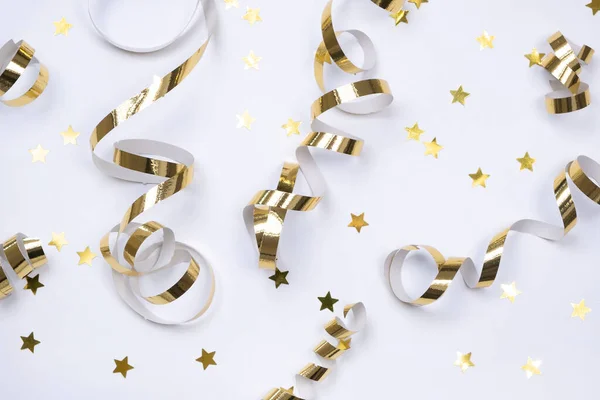 flat composition of golden ribbons or serpentine and golden confetti in the form of stars on a white background. The concept of a birthday, anniversary or holiday in golden colors.
