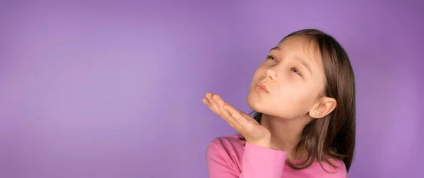 girl 8 years old sends an air kiss on a pink or purple background with a place to insert. copy space