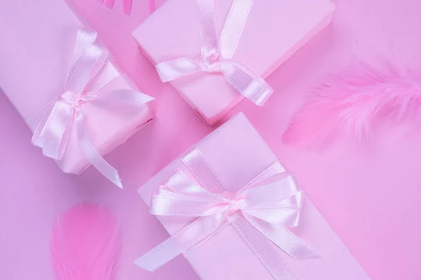 pink gift boxes with pink bows on a pink background decorated with feathers, top view, the concept of celebrating a girls birthday, party, anniversary in pink colors, or sale and shopping or a