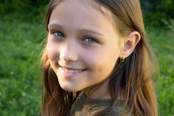 Güzel bir esmer kızın portresi kameraya bakıyor ve gülümsüyor, bir yaz günü yeşilliğin zeminine karşı sokakta duruyor. Genç meraklı çocuk gözlerini kaldırdı ve başını eğdi.