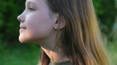 Küçük bir kızın portresi gökyüzüne bakıyor ve kafasını kameraya çeviriyor. Dışarıdaki rüya gibi doğa manzarası. Yüksek kalite 4k görüntü