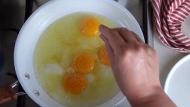 Bir kadın eli, dört kırık yumurtayı tavada tuzlar. Mutfak manzaralı. Yüksek kalite 4k görüntü
