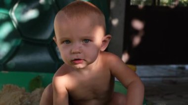 Bir bebek mutlu bir şekilde suyun yanındaki kumda oturuyor, gülüyor ve yüzlerinde bir gülümsemeyle oynuyor. Kumsalda boş zamanlarının tadını çıkarıyorlar. Mayoyla eğleniyorlar.