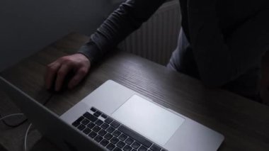 Gri elbiseli tanınmayan bir adam bir masada dizüstü bilgisayar kullanarak oturur ve fareyi kontrol eder. Uzaktan kumanda konsepti, serbest çalışma. Yüksek kalite 4k görüntü