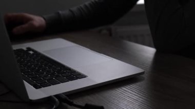 Tanımlanamayan gri elbiseli bir adam masada oturuyor karanlıkta dizüstü bilgisayar kullanıyor ve fareyi kontrol ediyor. Bilgisayar korsanlığı, para dolandırıcılığı, uzaktan çalışma, serbest çalışma. Yüksek kalite 4k görüntü