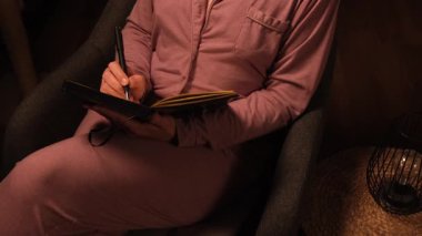 Pijamalarıyla sandalyede oturan bir kadın düşüncelerini bir günlüğe ya da günlük planlarına yazar. Yüksek kalite 4k görüntü