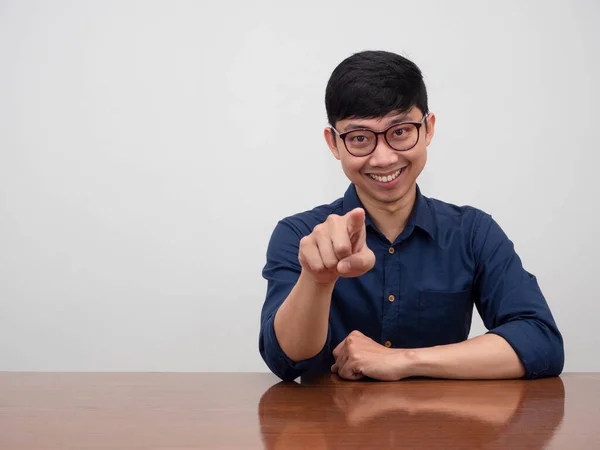 Positive asian businessman wear glasses sit at the desk confident smile point finger choosing you