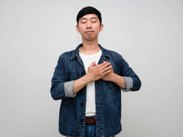 Positive asian man jeans shirt gesture hold his chest wish to peaceful isolated