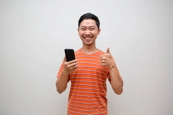 アジアの男オレンジ色のシャツは幸せな保持携帯電話と表示親指アップ絶縁 — ストック写真