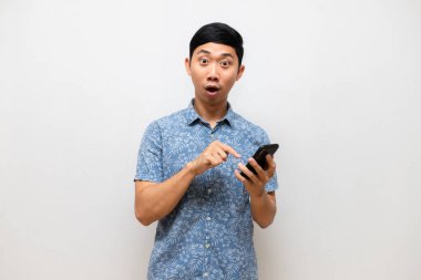 Asyalı erkek mavi gömleği heyecanlanıyor ve cep telefonuna işaret ediyor.