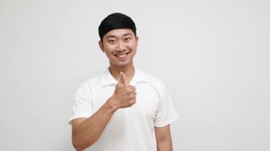 Olumlu genç Asyalı yakışıklı neşeli bir gülüş başparmağını beyaz arka planda göster.