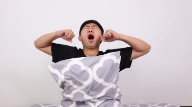 Asyalı adam uyanıyor, yastığa sarılıyor ve uykulu hissediyor.