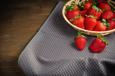 Gri masa örtüsü üzerinde sulu organik çilekler ve ahşap arka planda fotokopi alanı.