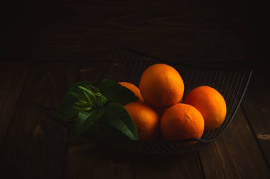 Koyu ahşap arka planda kırsal kasede mandalina portakalları..