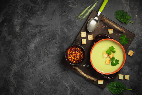 Healthy asparagus soup in a bowl over dark wooden cutting board, concrete background.