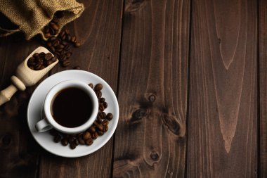 Koyu ahşap zemin üzerinde beyaz bir fincan espresso ile kavrulmuş kahve çekirdekleri.
