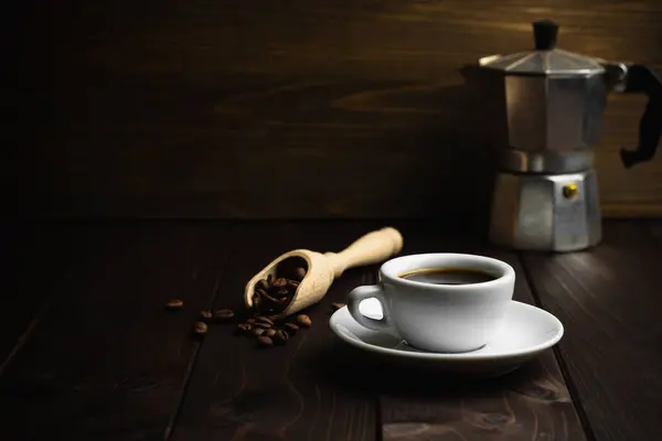 White cup of coffee with old metal coffee percolator on dark wooden background